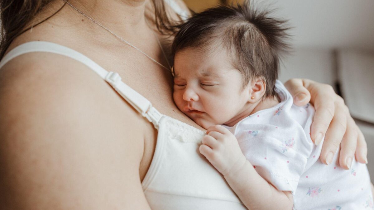 Amamentação e sono do bebê: recém-nascido dormindo durante a amamentação, representando o estudo japonês sobre duração do sono.