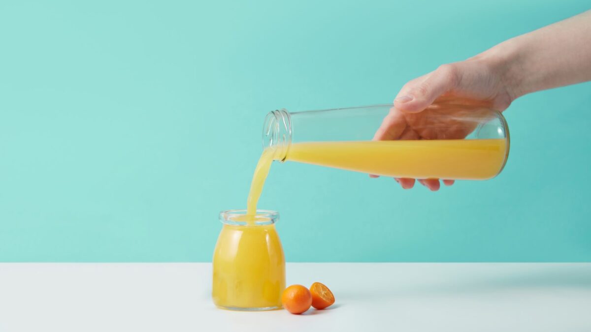 Copo de suco de laranja fresco ao lado de laranjas, ilustrando os benefícios do suco de laranja para a saúde.