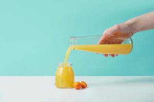 Copo de suco de laranja fresco ao lado de laranjas, ilustrando os benefícios do suco de laranja para a saúde.