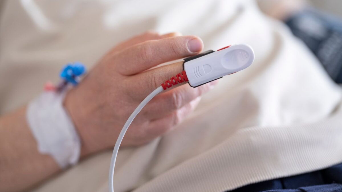 Titulação automática de oxigênio: paciente internado com oxímetro de pulso no dedo e monitor de saturação ao lado do leito.