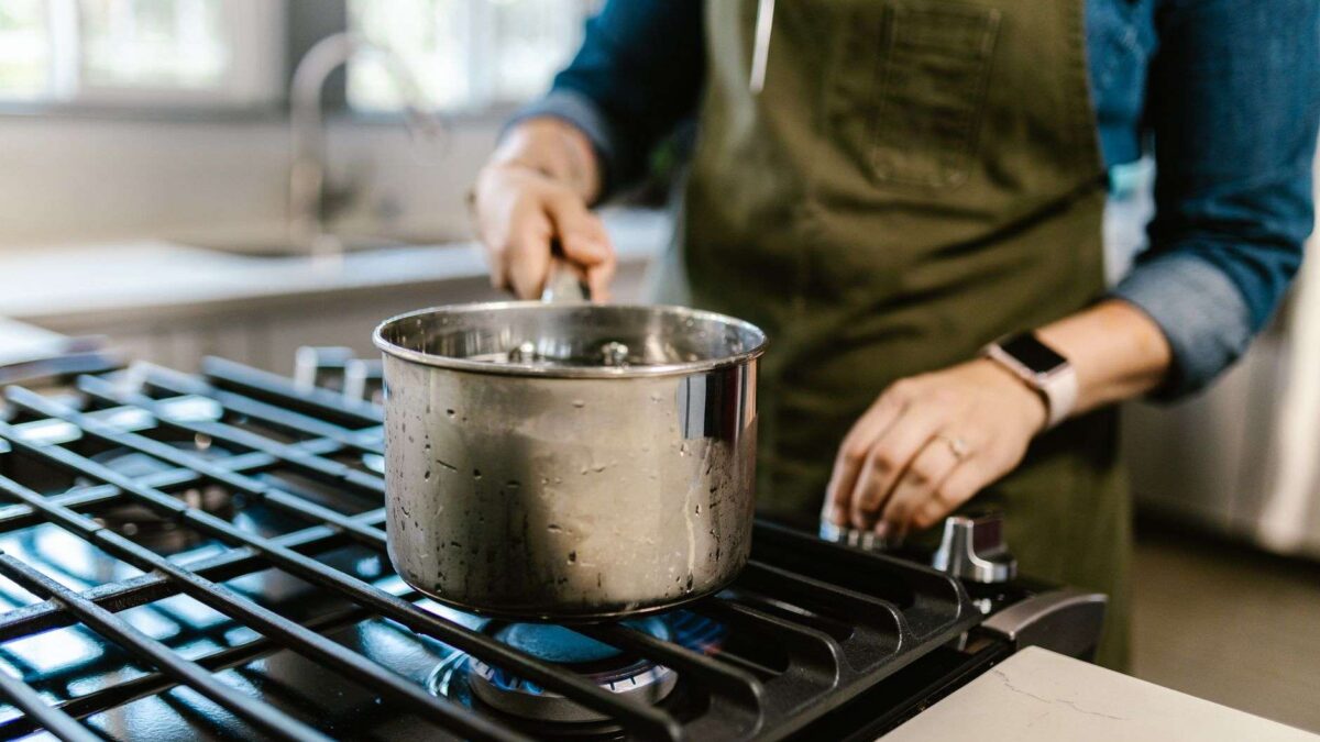 Mulher de avental cozinhando com panela sobre fogão a gás em uma cozinha doméstica aconchegante