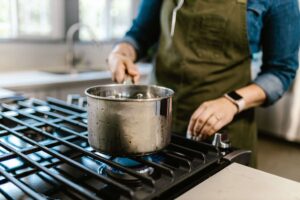 Mulher de avental cozinhando com panela sobre fogão a gás em uma cozinha doméstica aconchegante